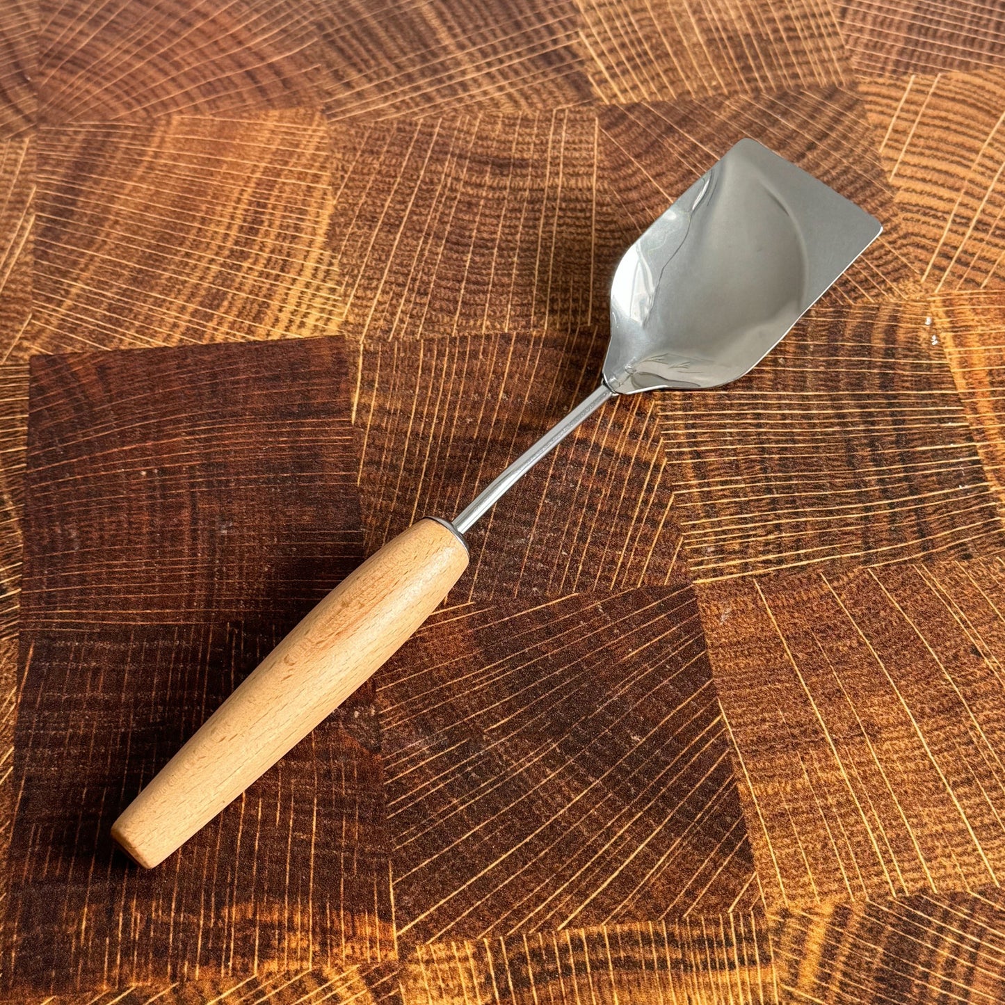Stainless steel spoon with a scrape edge with a wood handle on a wood surface.