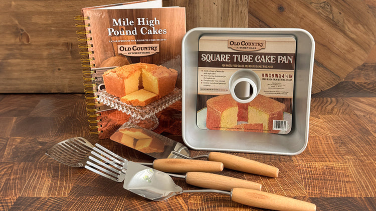A photo of a cookbook, square cake pan, and vintage-style utensils on a wood background