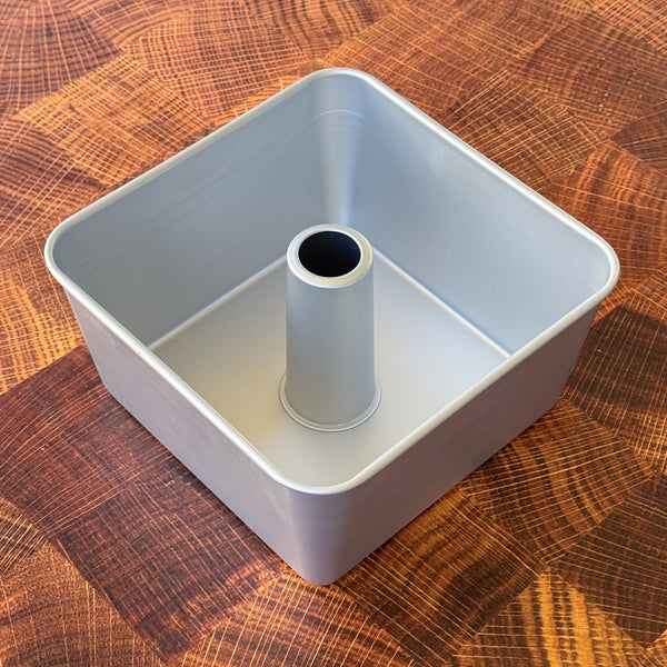 A square tube cake pan made of aluminum, displayed on a wooden surface.