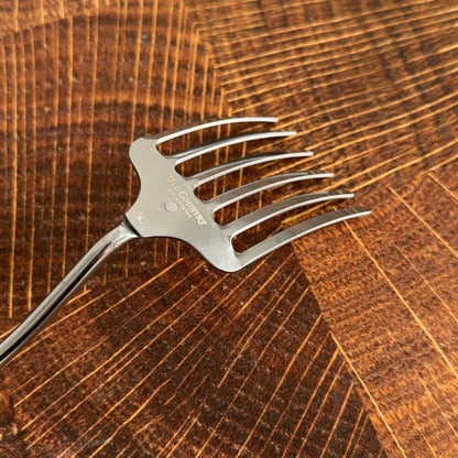 A close up of a metal mixing fork with wooden handle on a wooden surface