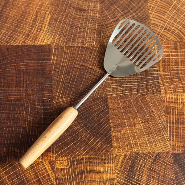Metal slotted scoop with wooden handle on a wooden surface