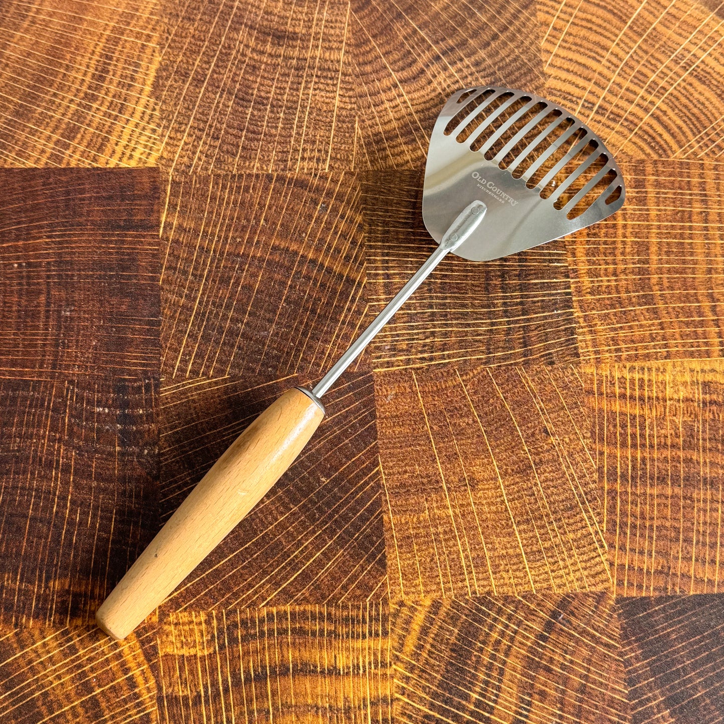 Metal slotted spoon with wooden handle on a wooden cutting board